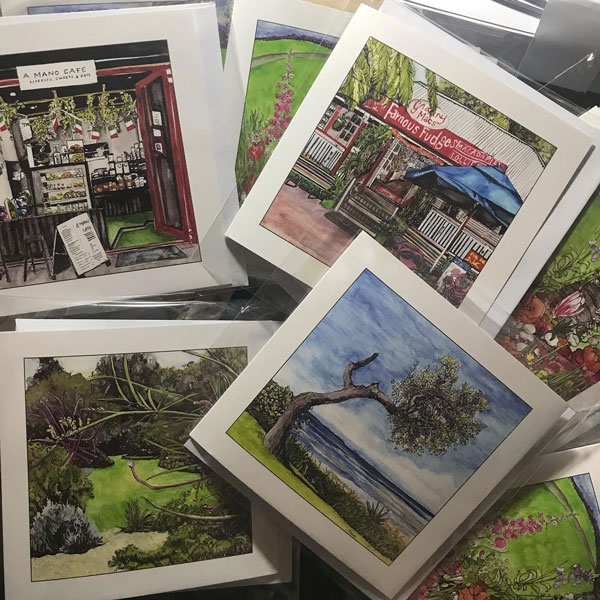 Assortment of products featuring custom illustrations, including framed artworks, cards, and calendars. The images showcase various scenes such as a café storefront, local landscapes, and gardens, highlighting the diverse range of artwork available in the shop.