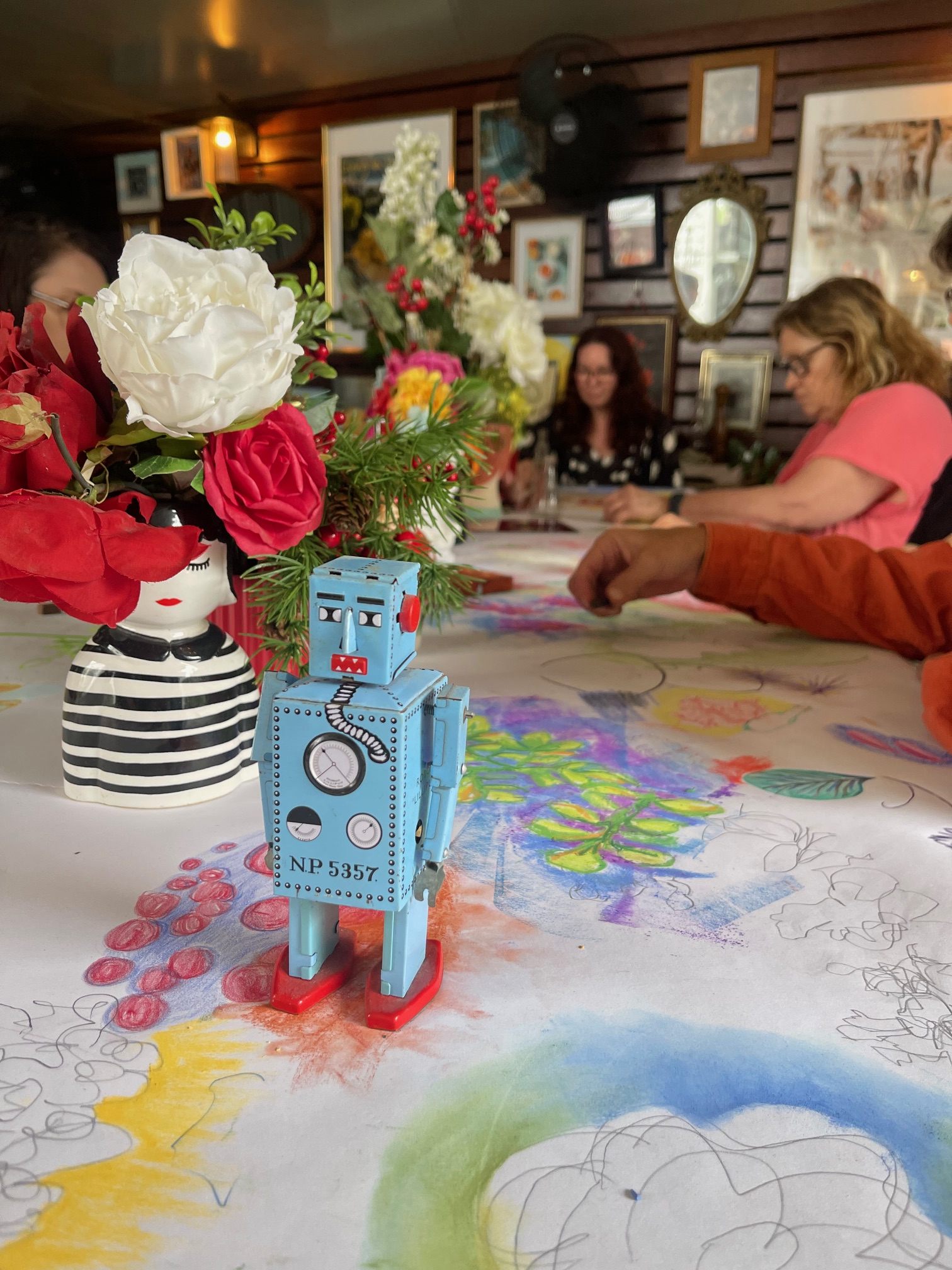 Workshop table scene with flowers, a small blue robot, and colourful drawing experiments
