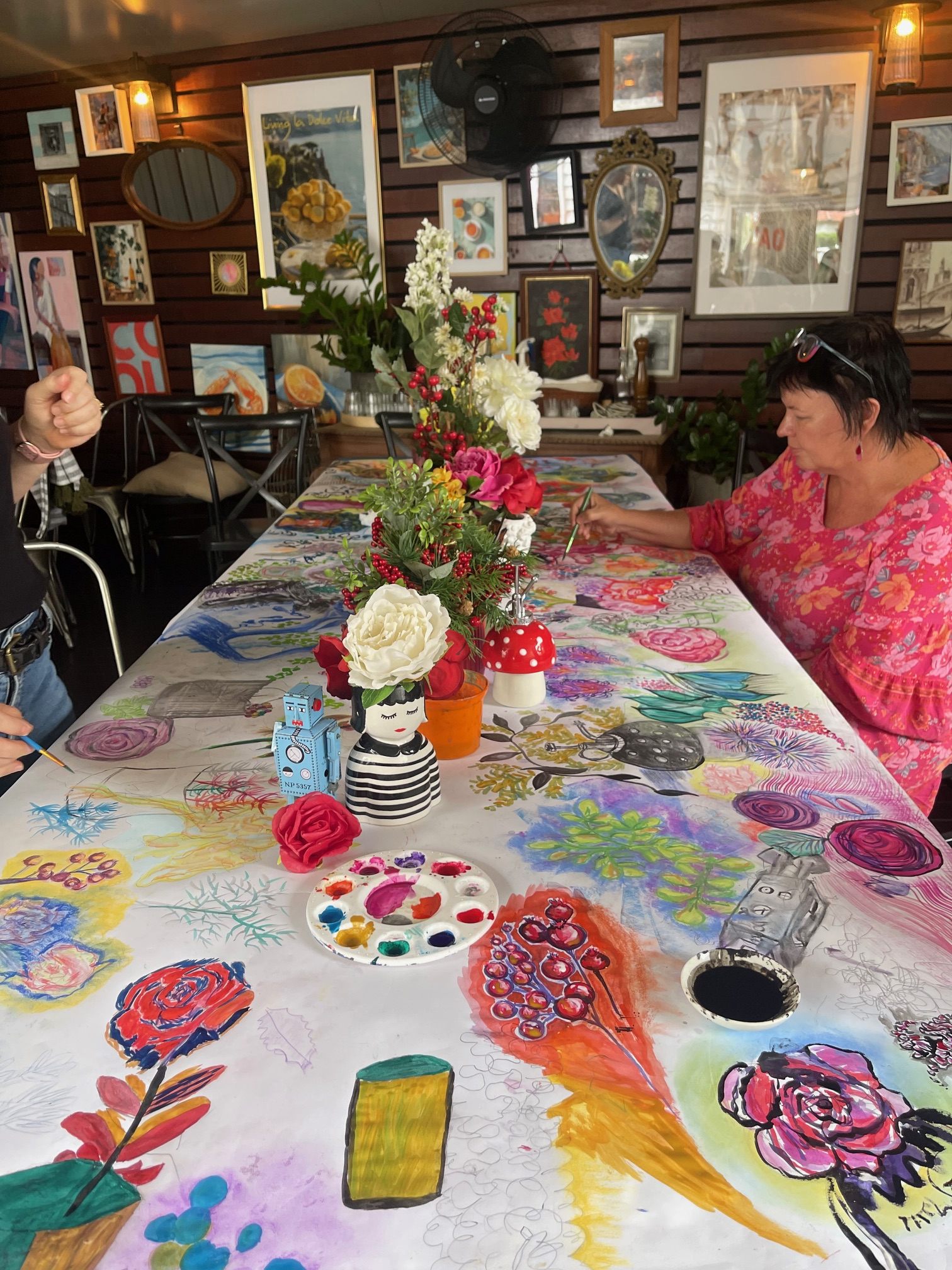 Long view down the workshop table with participants drawing and painted materials spread out
